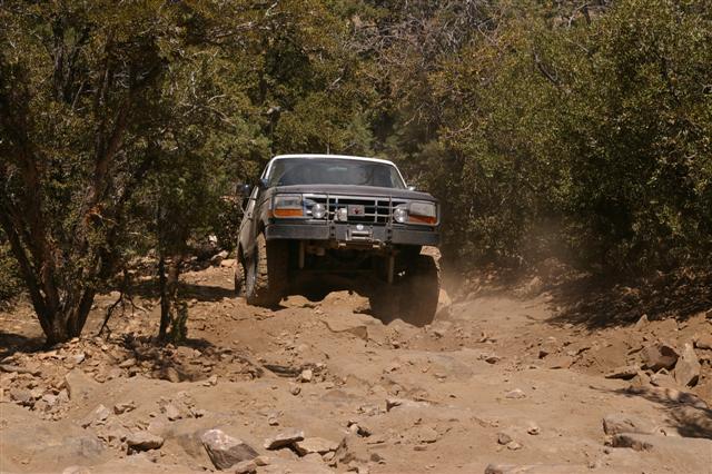 Front view of a black 1992 Ford Bronco off-roading on a dusty, rocky trail