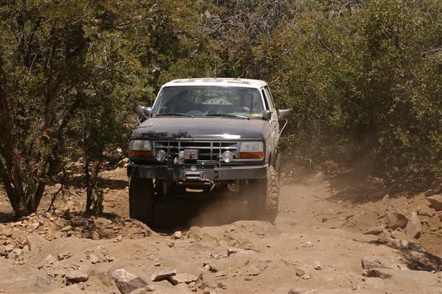 Dark gray and white Ford Bronco off-roading on a dirt path, kicking up dust