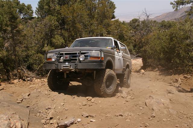 Modified Ford Bronco with aftermarket bumper and lift kit driving on a rocky dirt trail