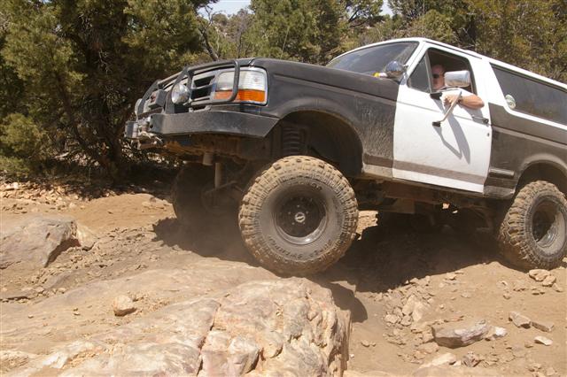 Two-tone Ford Bronco with aftermarket bumper and large tires navigating a rocky trail