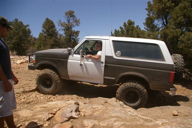 Two-tone Ford Bronco navigating rocky terrain with driver and passenger visible