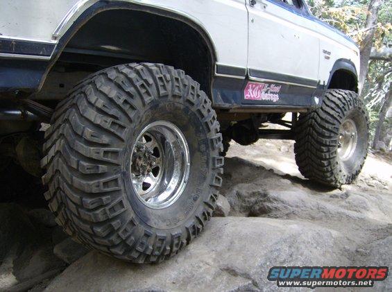 Big tires on a lifted SUV climbing over rocks. Sticker on the side says "XO-National Garage"