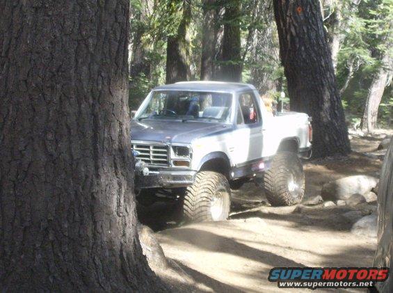 Gray and white Ford F-Series pickup truck with large tires driving off-road