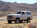 1996 Ford Bronco - This 1996 Ford Bronco is captured in a three-quarter front view, parked on a dirt road with a mountainous backdrop.