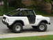 1996 Ford Bronco - This white Ford Bronco features a soft top, roll cage, and off-road tires, parked curbside.