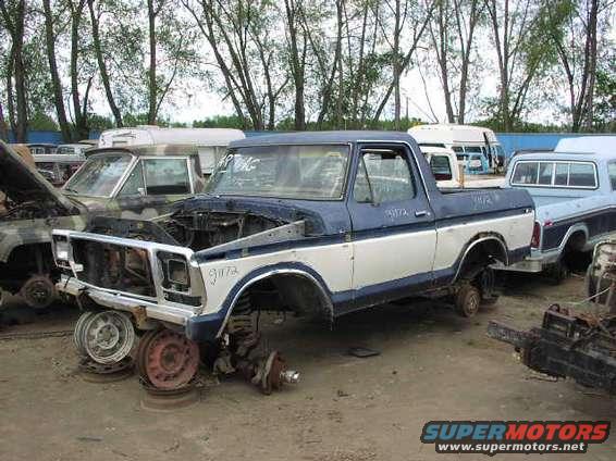 Two-tone blue and white pickup truck missing wheels, hood open. 1979 model