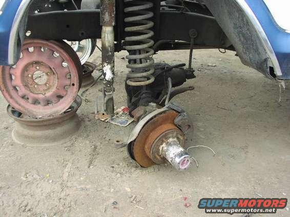 close-up of a vehicle's front suspension with a missing wheel, showing the brake rotor and hub assembly