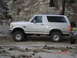 1996 Ford Bronco - A silver 1996 Ford Bronco is parked on a dirt road with rocky hills in the background.