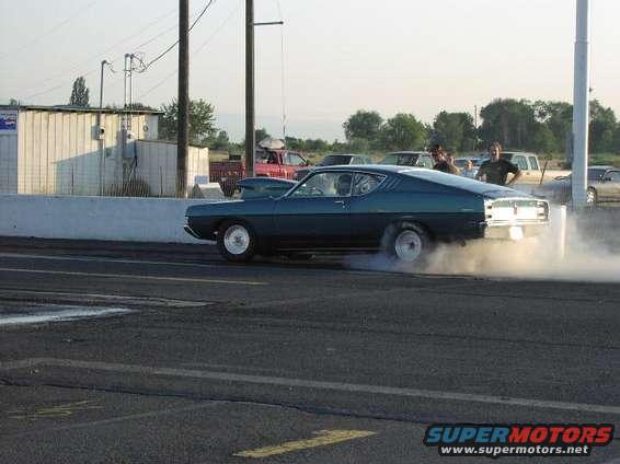 Blue coupe doing a burnout on a drag strip with smoke billowing