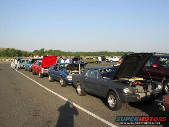 Dark gray coupe with hood open, number C610 on door, parked in line at drag strip