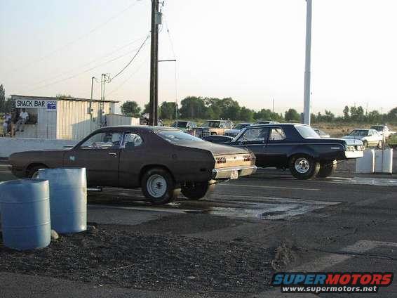 Brown 1970s coupe and blue 1970s coupe on drag strip, snack bar in background