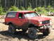 1979 Ford Bronco - Mud-covered red 1987 Ford Bronco navigates off-road terrain.