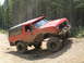 1979 Ford Bronco - This lifted red SUV with large tires navigates a steep dirt incline amidst a forest.