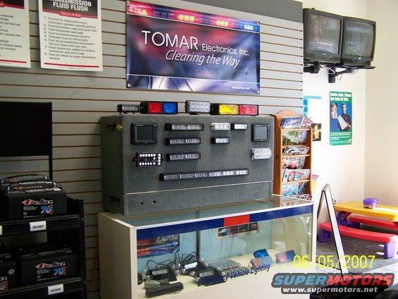 Display of TOMAR Electronics emergency lights and vehicle lighting equipment, with batteries on a shelf and a date stamp of 06/05/2007