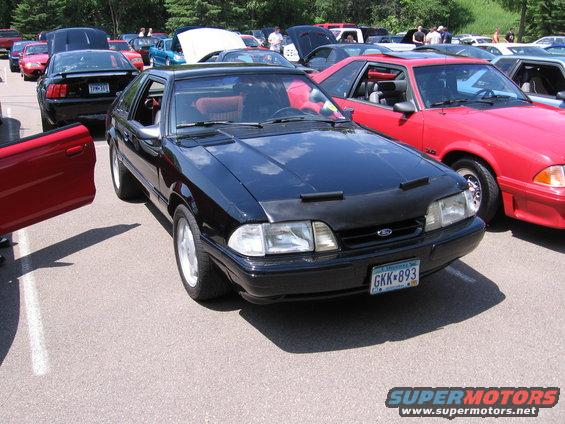 Black Ford Mustang with a black car bra and red interior, parked at an outdoor car show