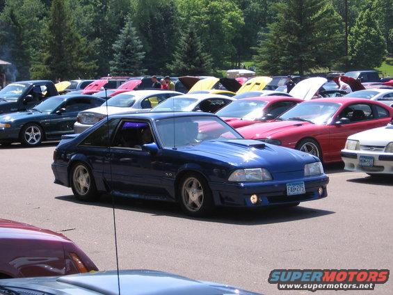 Blue 1989 Ford Mustang with a hood scoop and 5.0 badge, parked in a lot with other cars
