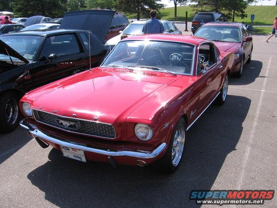 Red classic Ford Mustang with chrome grille and bumper, parked in lot. License plate reads 1966