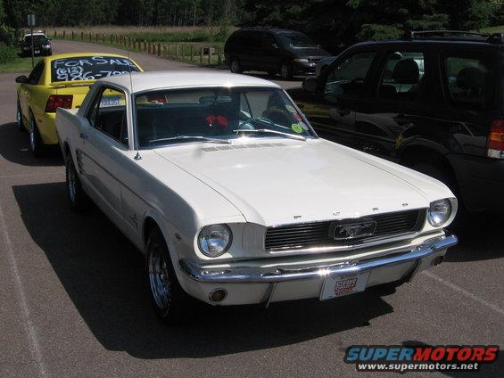 White classic Mustang parked next to a yellow car with a 'For Sale' sign