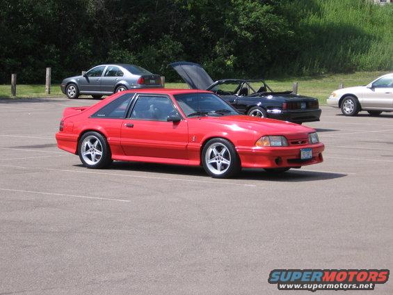 Red coupe with a body kit and five-spoke wheels parked in a lot