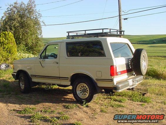 Tan 1988 Ford Bronco with roof rack and rear spare tire, seen from 3/4 front