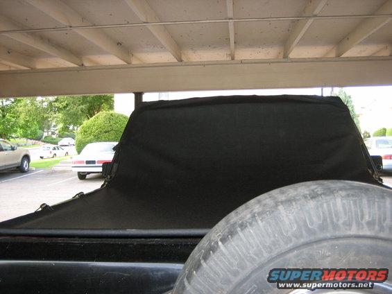 Back of a truck with a black cover over the bed and a spare tire visible. Other cars parked nearby
