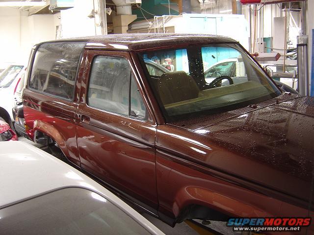 1986 Ford Bronco II in a workshop, showing the side and front quarter view. The vehicle has a brown metallic paint job with water droplets on the surface