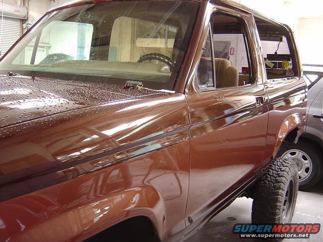 Brown 1986 Ford Bronco II, side view showing front fender, door, and rear quarter panel. Some water droplets on the hood