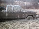 Side view of a 1990 Ford Ranger covered in mud, stuck in a muddy field