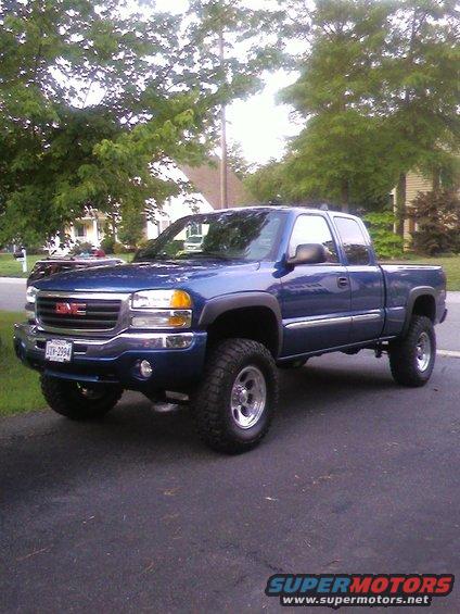 Blue GMC Sierra pickup truck with lifted suspension and off-road tires, parked on asphalt
