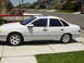 1995 Ford Taurus - Side profile of a white 1995 Ford Taurus sedan parked on a suburban driveway.