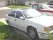 1995 Ford Taurus - A white 1995 Ford Taurus sedan is parked in a driveway, with a red and white pickup truck behind it.