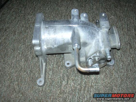 Aluminum intake manifold with metal tubing attached, resting on a carpeted surface