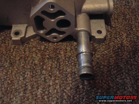 Close-up of a metal automotive part with a hose barb, resting on a brown carpet