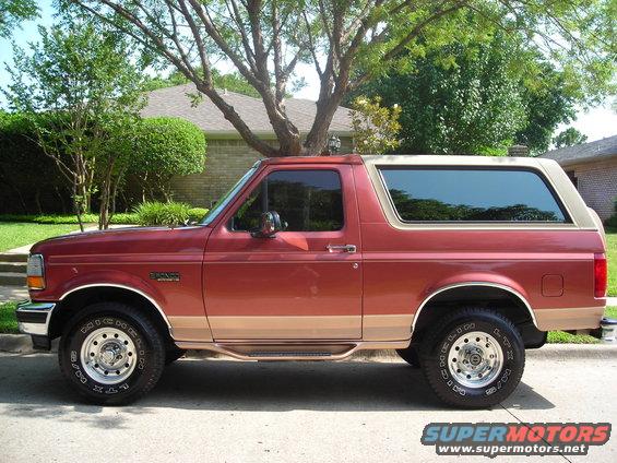 Red and tan Ford Bronco SUV parked on a residential street, side view