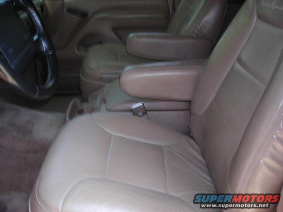 Front seats and center console of a vehicle. Beige leather seats with armrests. Steering wheel visible on the left