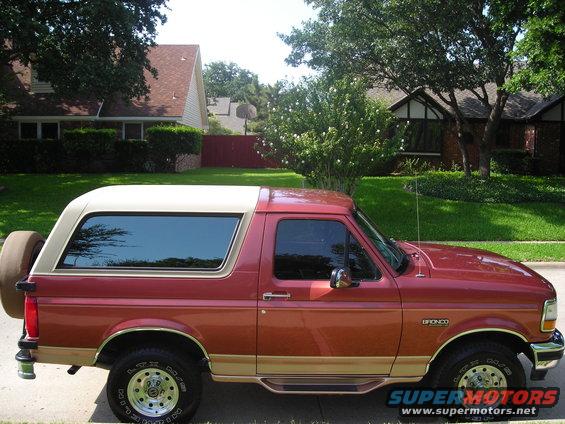 Red and tan Ford Bronco SUV, side view, spare tire on rear door, parked in residential area