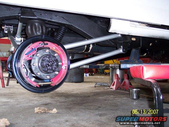 Rear axle assembly with red brake shoes and silver suspension arms, under a white vehicle