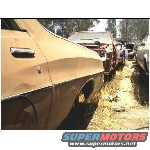 Several old cars parked in a grassy lot. One car in foreground is rusty brown
