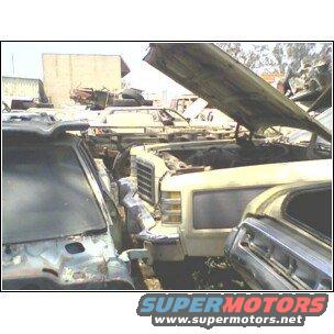 Several old cars crammed together in a junkyard, one with hood open