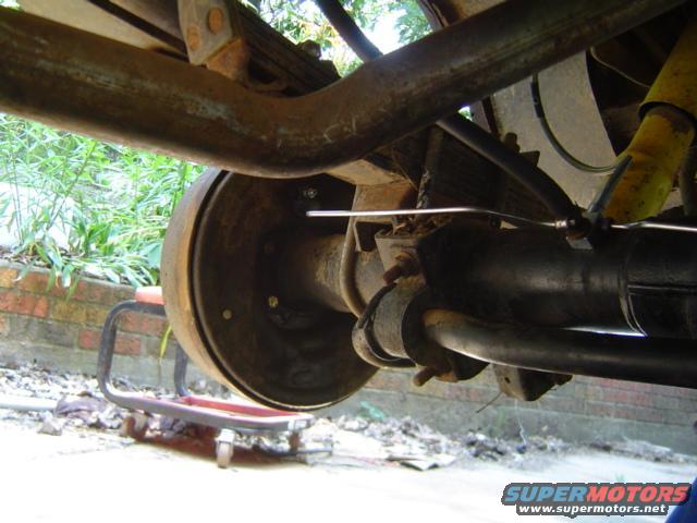 Close-up of a vehicle's rear axle, drum brake, leaf springs, and yellow shock absorber