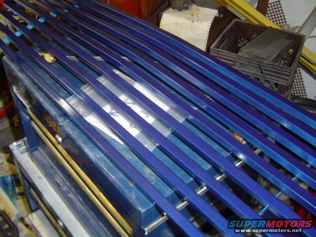 Blue metal bars stacked on top of a blue toolbox. Some plastic-wrapped items are visible underneath the bars