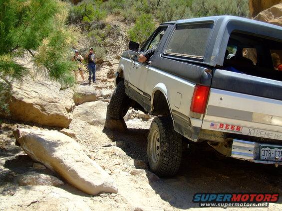 1987 Ford Bronco navigating a rocky off-road trail with two people standing nearby