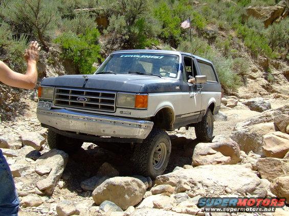 1987 Ford Bronco navigating a rocky trail, front passenger side visible, hand waving from driver's window
