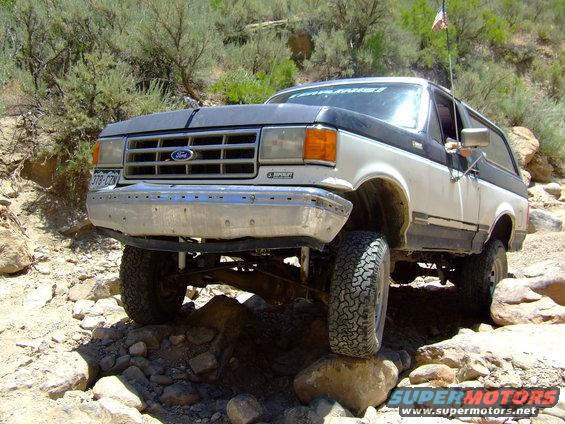 White and black 1987 Ford Bronco on rocky terrain, front driver's side tire elevated
