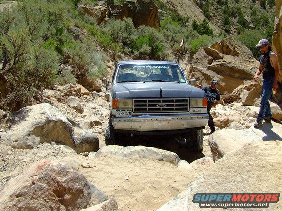 1987 Ford Bronco navigating a rocky trail with two people standing nearby
