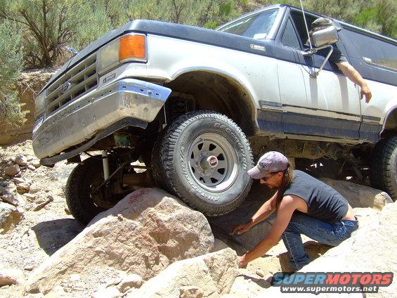 1987 Ford Bronco navigating rocky terrain with a person guiding