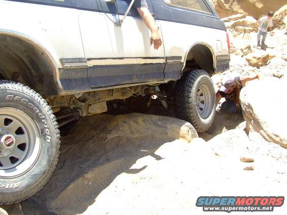 White Ford Bronco navigating rocky terrain, driver's arm out the window