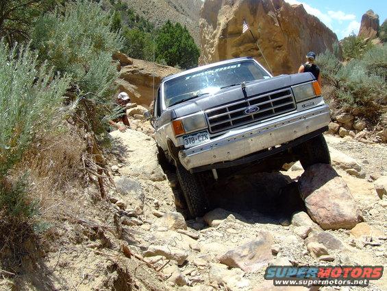 1987 Ford Bronco navigating a rocky off-road trail with a person visible in the background