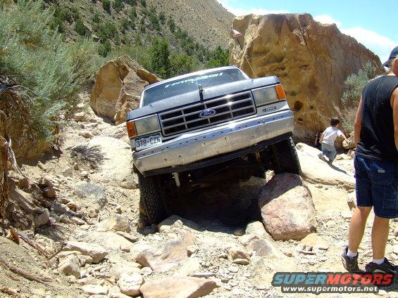 Ford truck navigating a rocky trail, front end angled up over a boulder