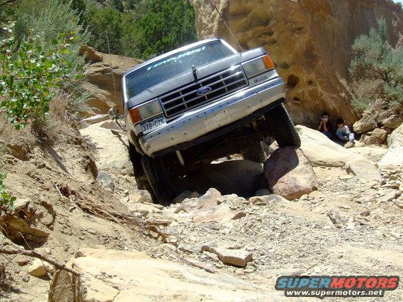 Silver 1987 Ford Bronco navigating a rocky trail, front-left tire elevated